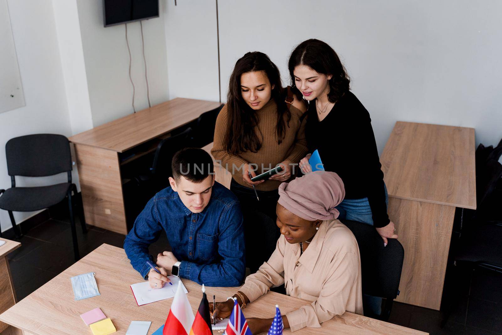 Multiethnic students and teacher study foreign languages together in class. Studing with notebook. Black attractive girl student study with white people together and look into camera. by Rabizo