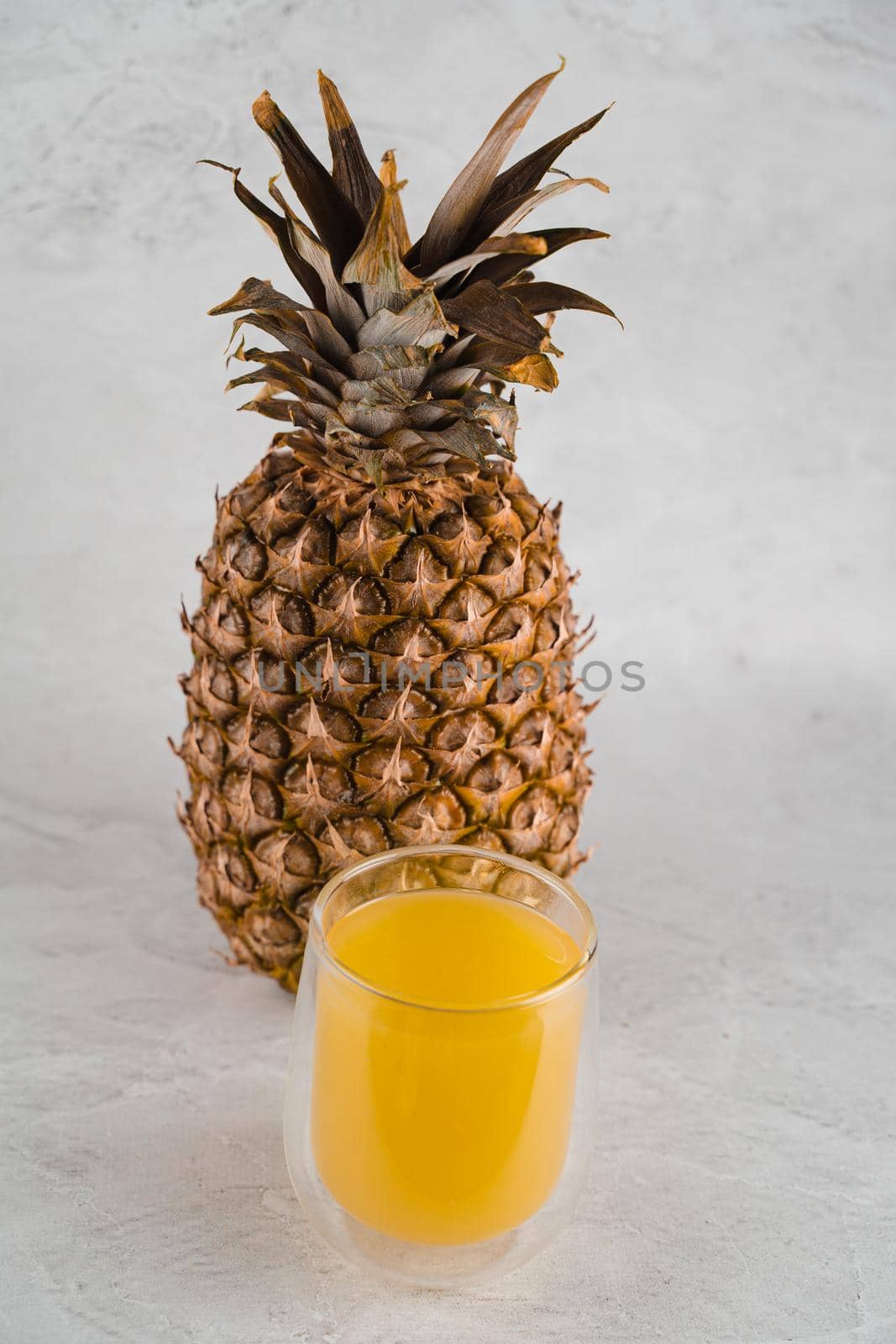 Pineapple fruit and juice in double glass cup on white stone background. Pouring yellow tropical fruit juice into glass. by Rabizo