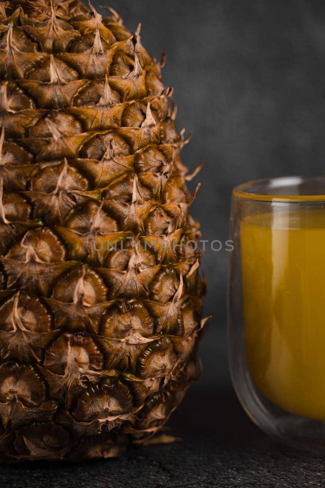 Pineapple fruit and juice in double glass cup on black stone background. Pouring yellow tropical fruit juice into glass.