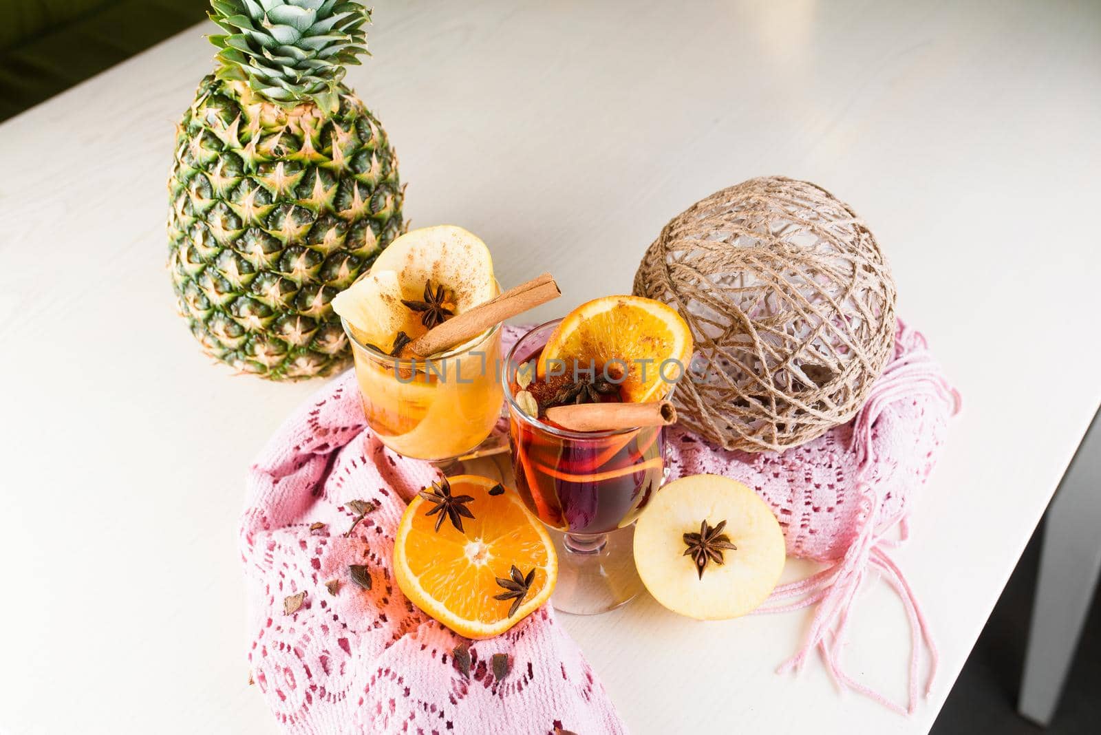 Mulled wine, grog and punch hot alcohol drinks on the table with seasonal decoration: pineapple, cinnamon, apple, orange, star anise. Seasonal spiced drink.