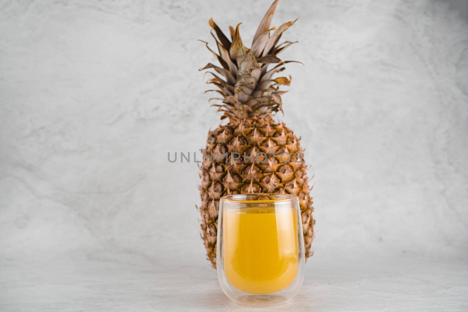 Pineapple fruit and juice in double glass cup on white stone background. Pouring yellow tropical fruit juice into glass. by Rabizo