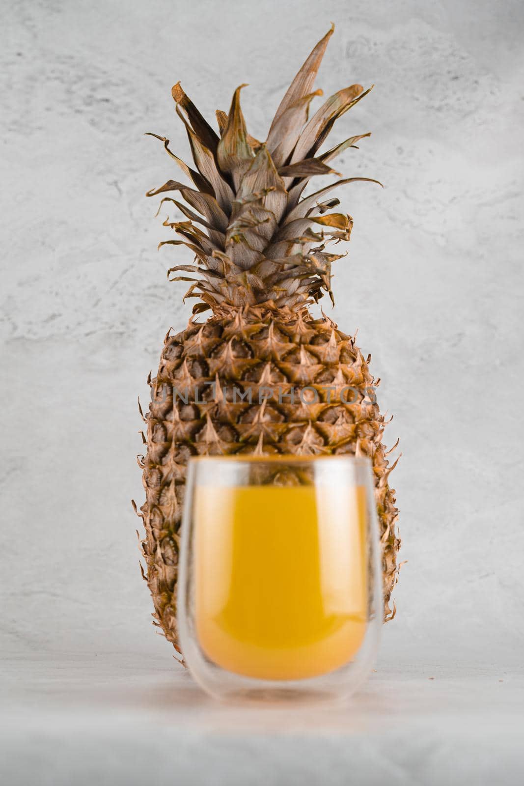 Pineapple fruit and juice in double glass cup on white stone background. Tropical fruit Pouring yellow tropical juice into glass.