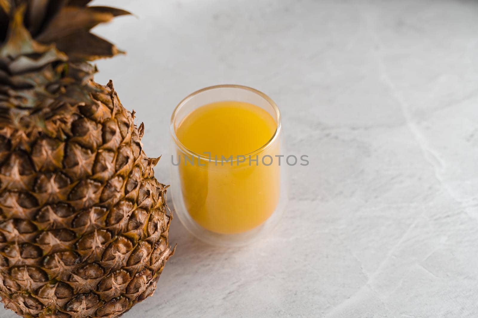 Pineapple fruit and juice in double glass cup on white stone background. Tropical fruit Pouring yellow tropical juice into glass.