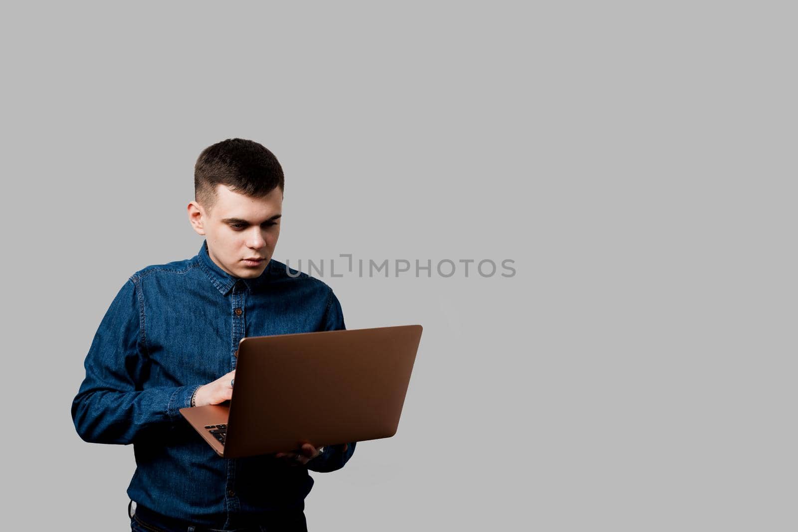 Handsome man with laptop on the gray background. Business man working online at home by Rabizo