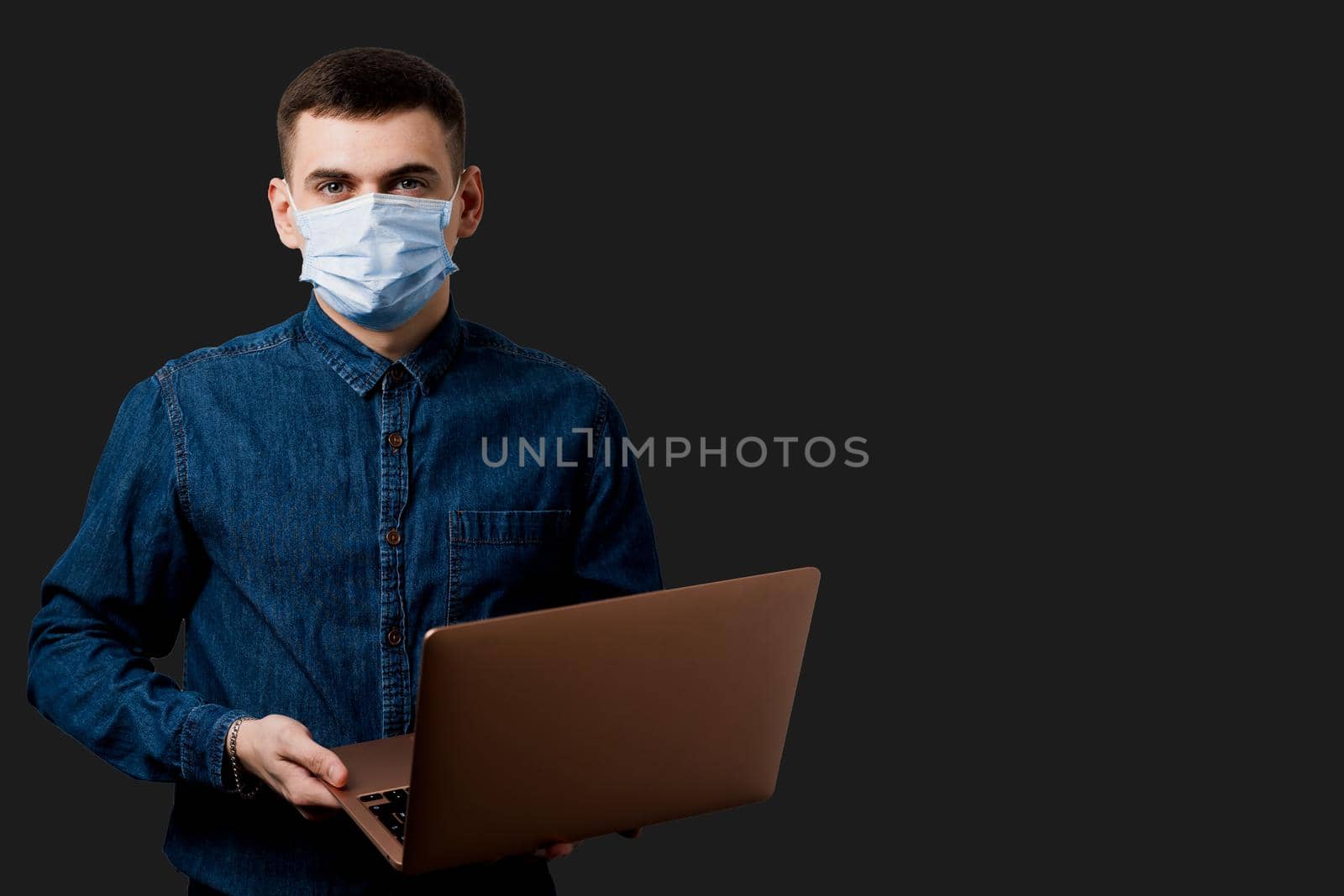 Education and working on-line at quarantine coronavirus covid-19 period. Man in medical mask with laptop on black background.