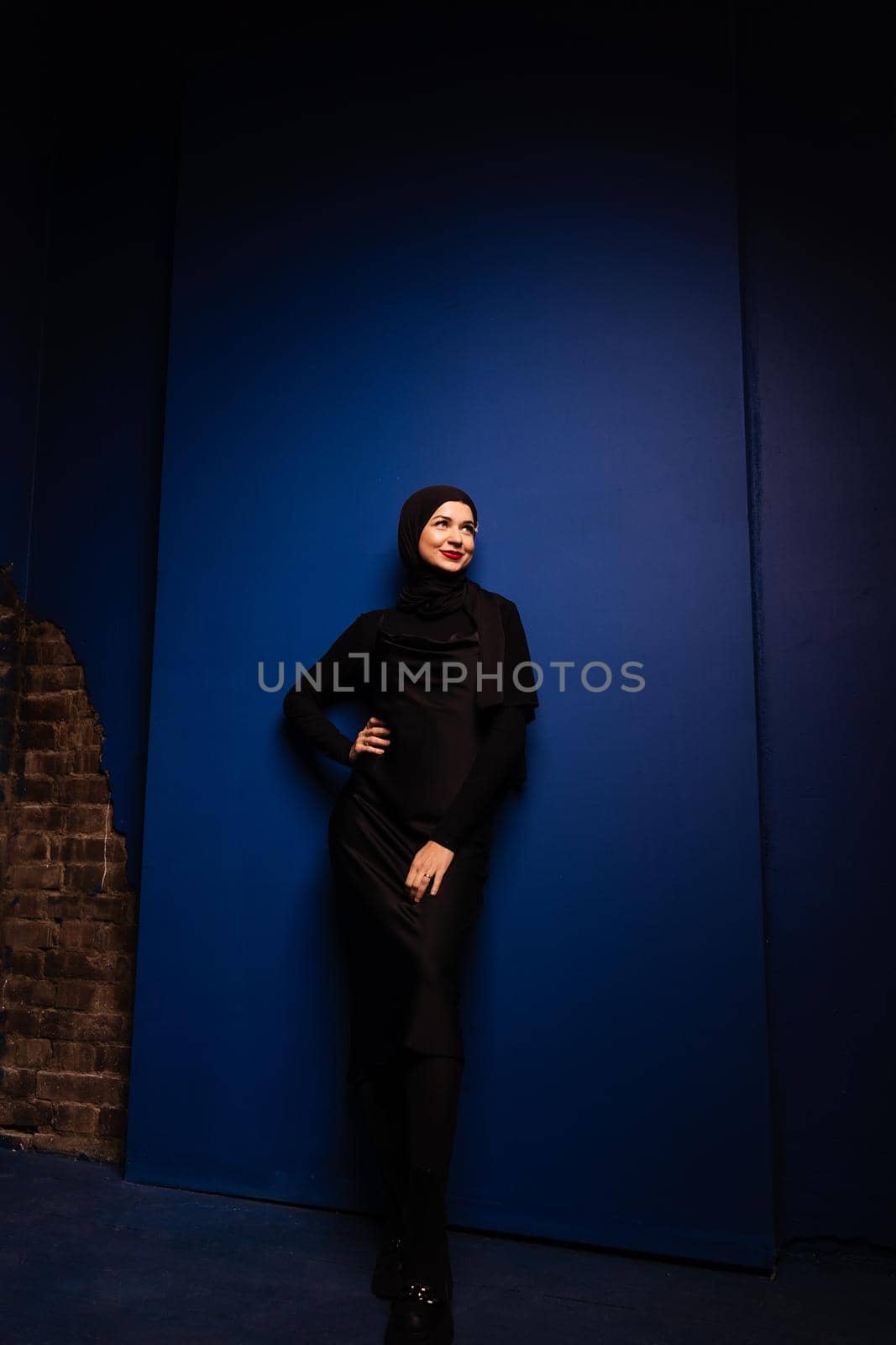 Fashion muslim woman in black hijab is posing on blue background in studio. Professional caucasian model. by Rabizo