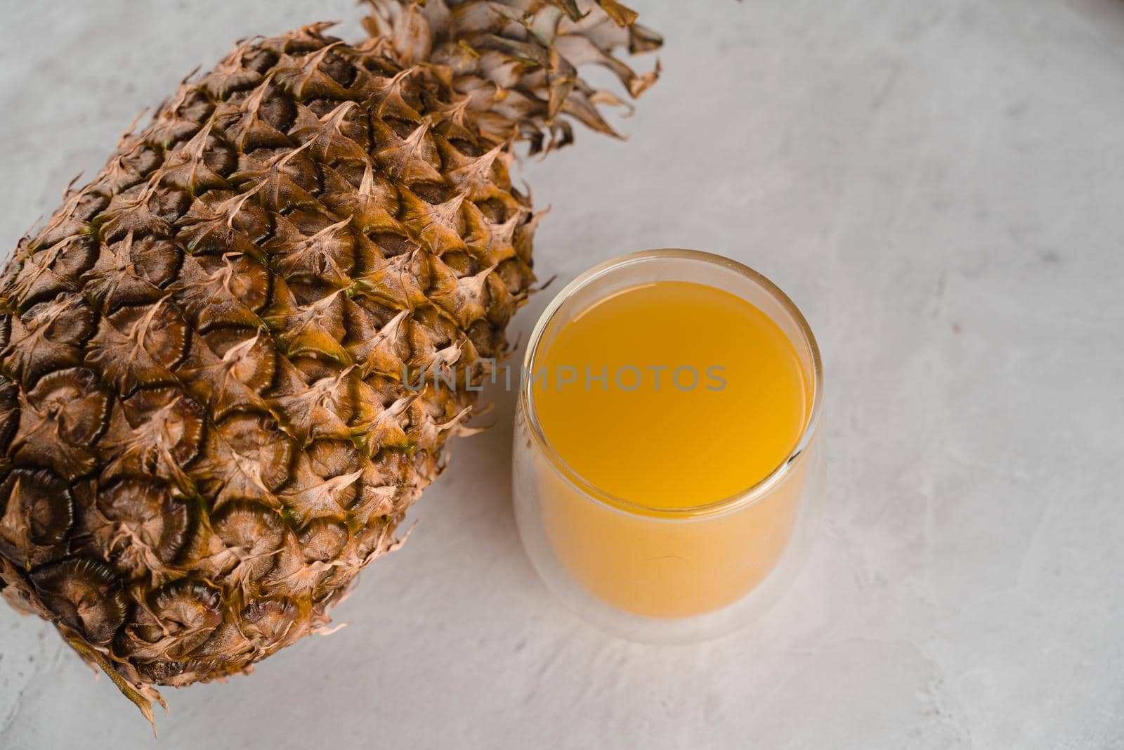 Pineapple fruit and juice in double glass cup on white stone background. Tropical fruit Pouring yellow tropical juice into glass.