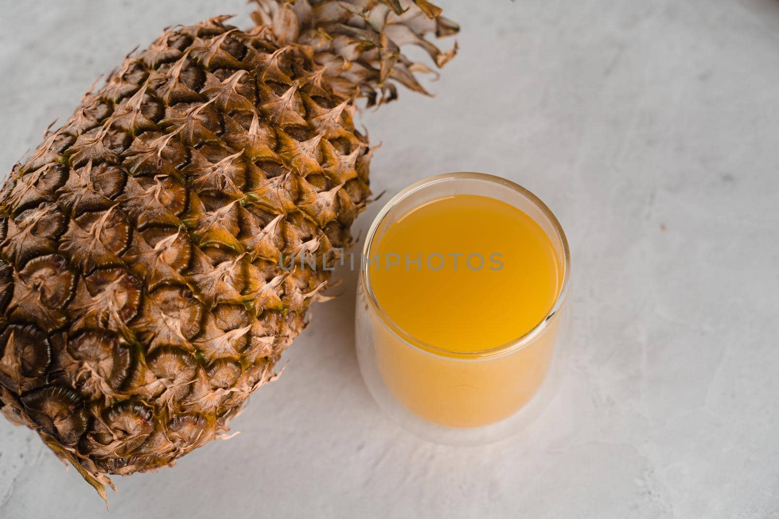 Pineapple fruit and juice in double glass cup on white stone background. Pouring yellow tropical fruit juice into glass. by Rabizo