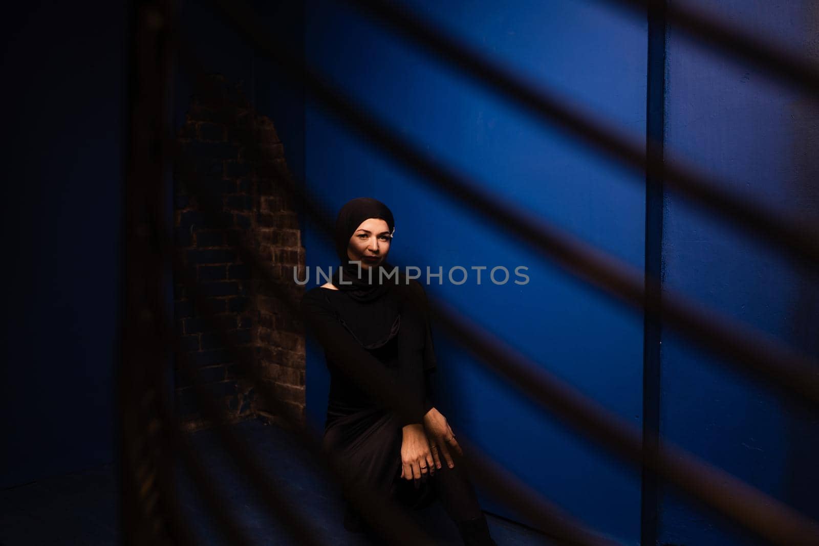 Fashion muslim model in black hijab is posing on blue background in studio. Islam religion creative photo.