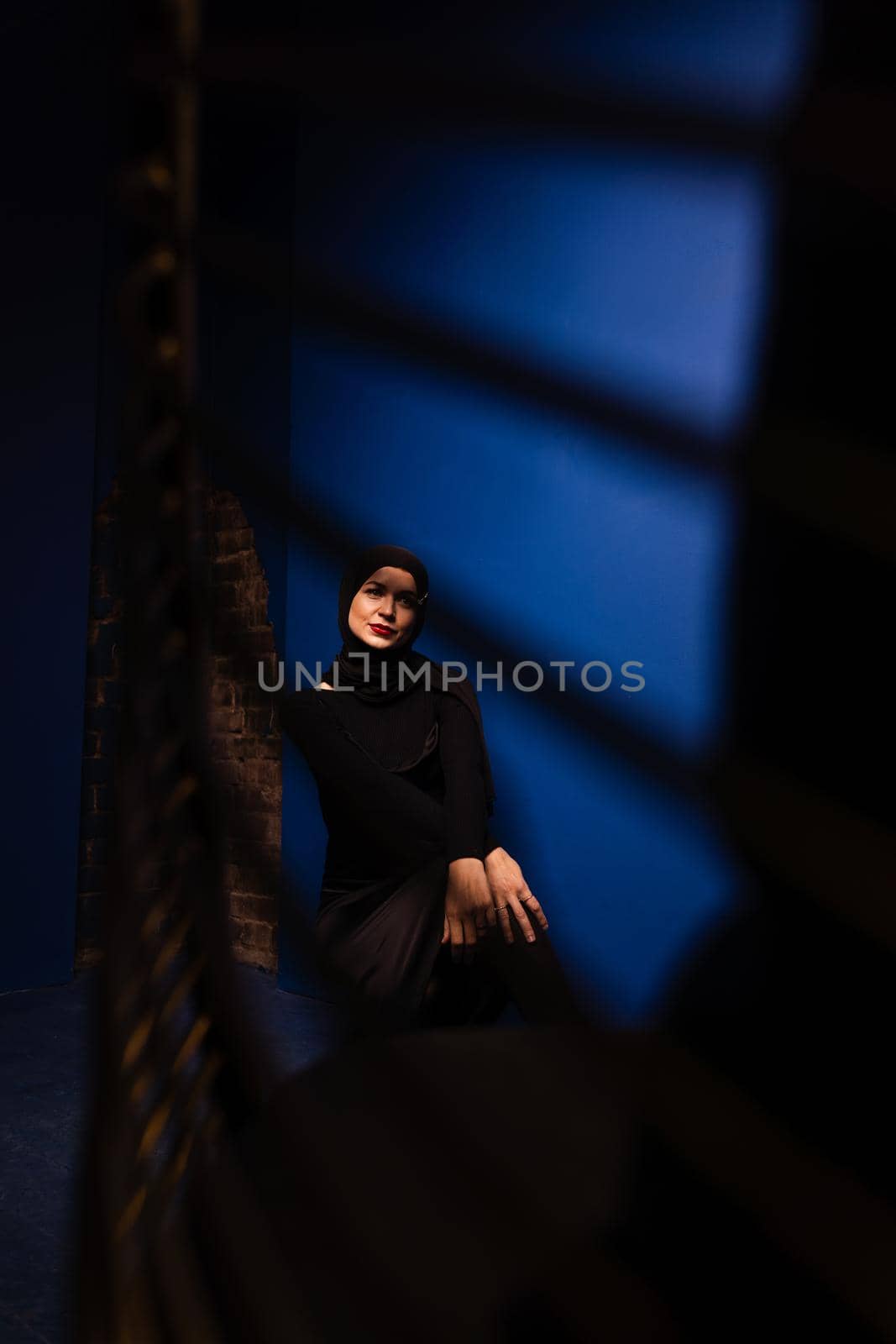 Fashion muslim model in black hijab is posing on blue background in studio. Islam religion creative photo.