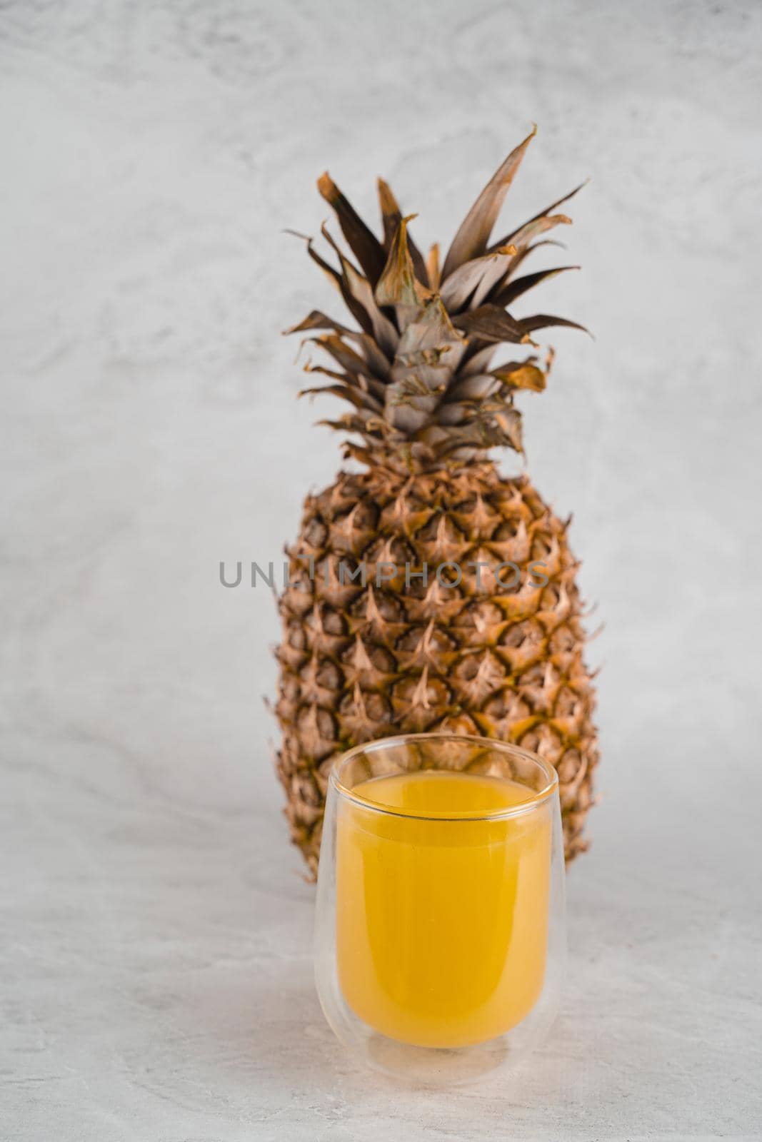 Pineapple fruit and juice in double glass cup on white stone background. Tropical fruit Pouring yellow tropical juice into glass.