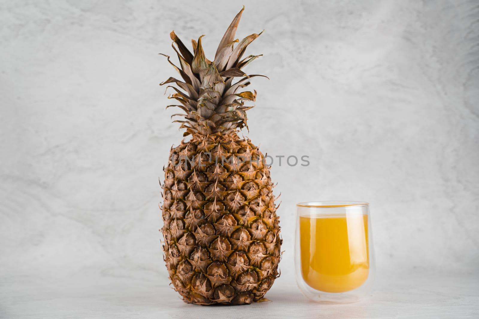 Pineapple fruit and juice in double glass cup on white stone background. Tropical fruit Pouring yellow tropical juice into glass.