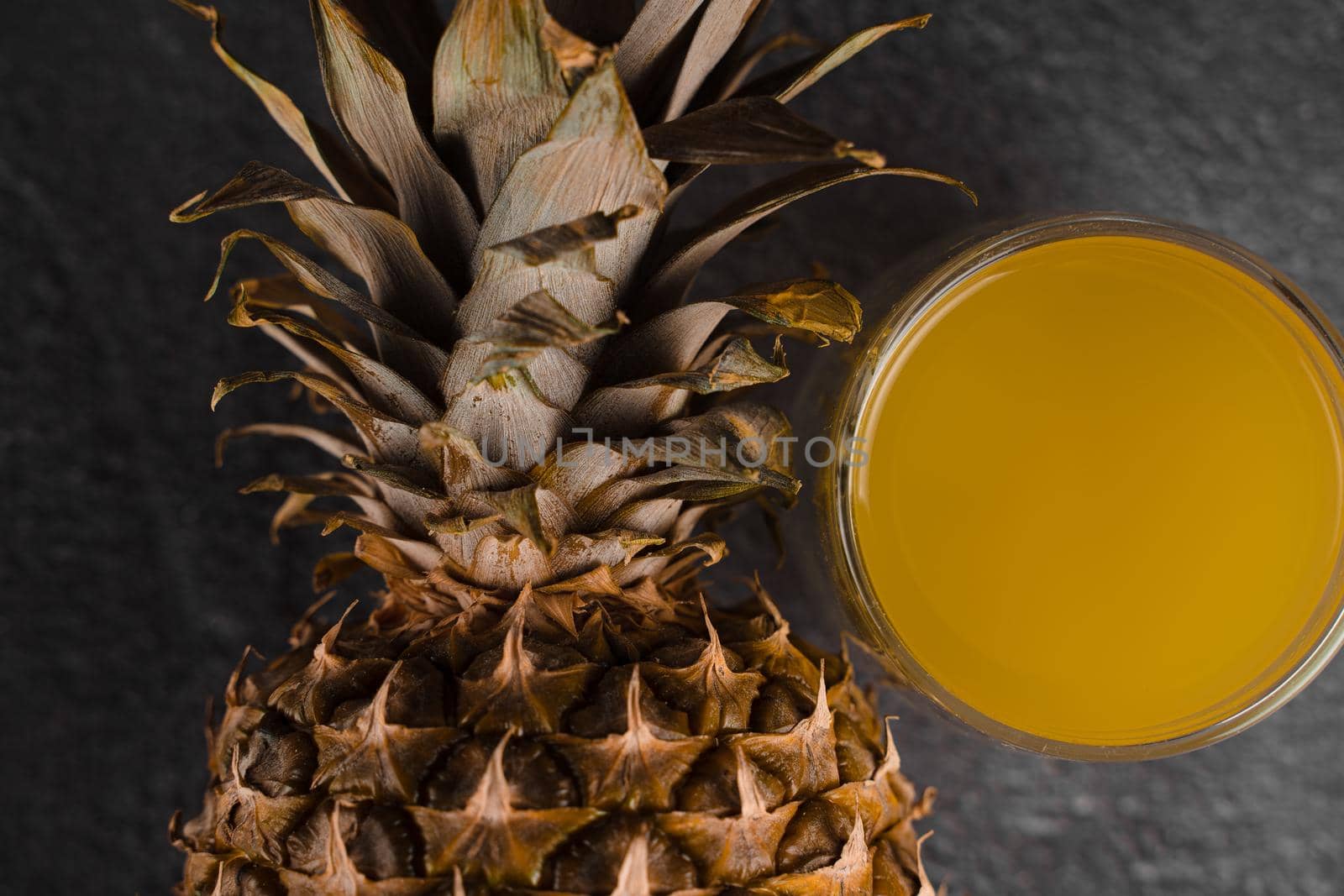 Pineapple fruit and juice in double glass cup on black stone background. Pouring yellow tropical fruit juice into glass.