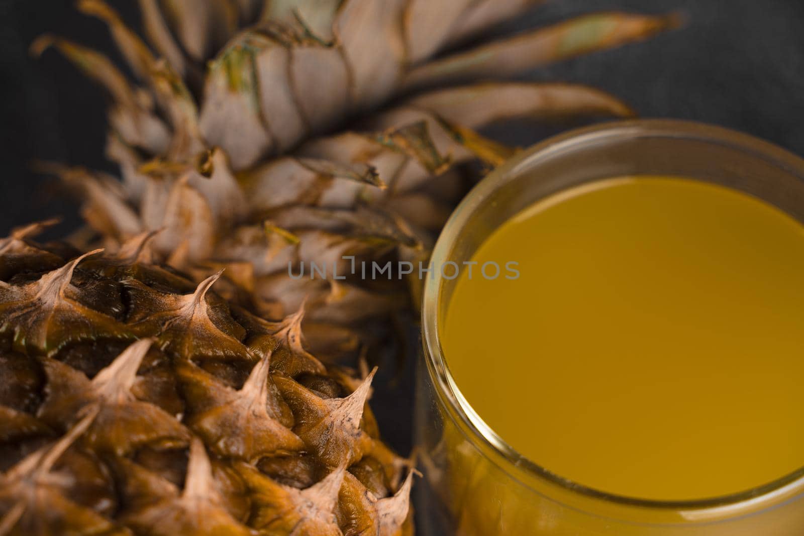 Pineapple fruit and juice in double glass cup on black stone background. Pouring yellow tropical fruit juice into glass by Rabizo