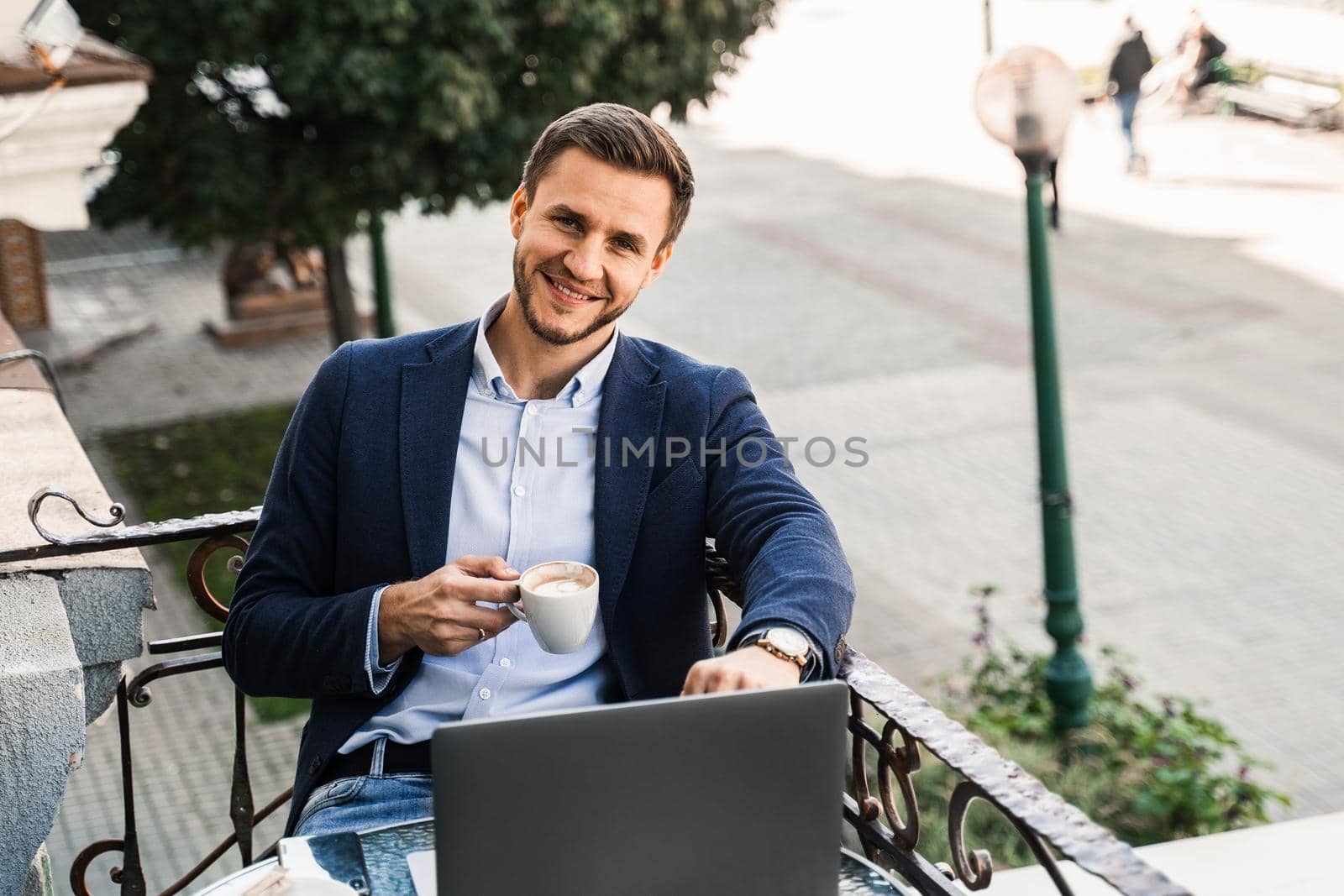 Handsome man with cup of coffee is working online using laptop in cafe. Remote work