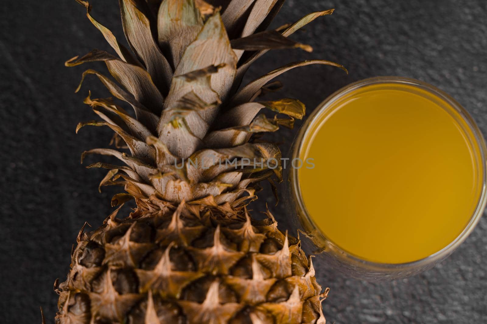 Pineapple fruit and juice in double glass cup on black stone background. Pouring yellow tropical fruit juice into glass.