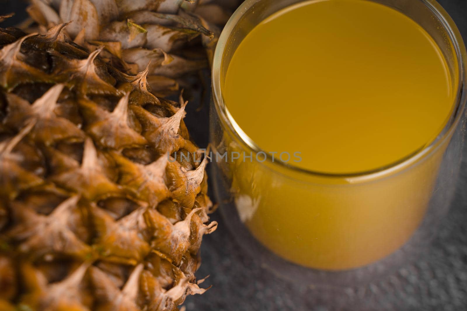 Pineapple fruit and juice in double glass cup on black stone background. Pouring yellow tropical fruit juice into glass by Rabizo