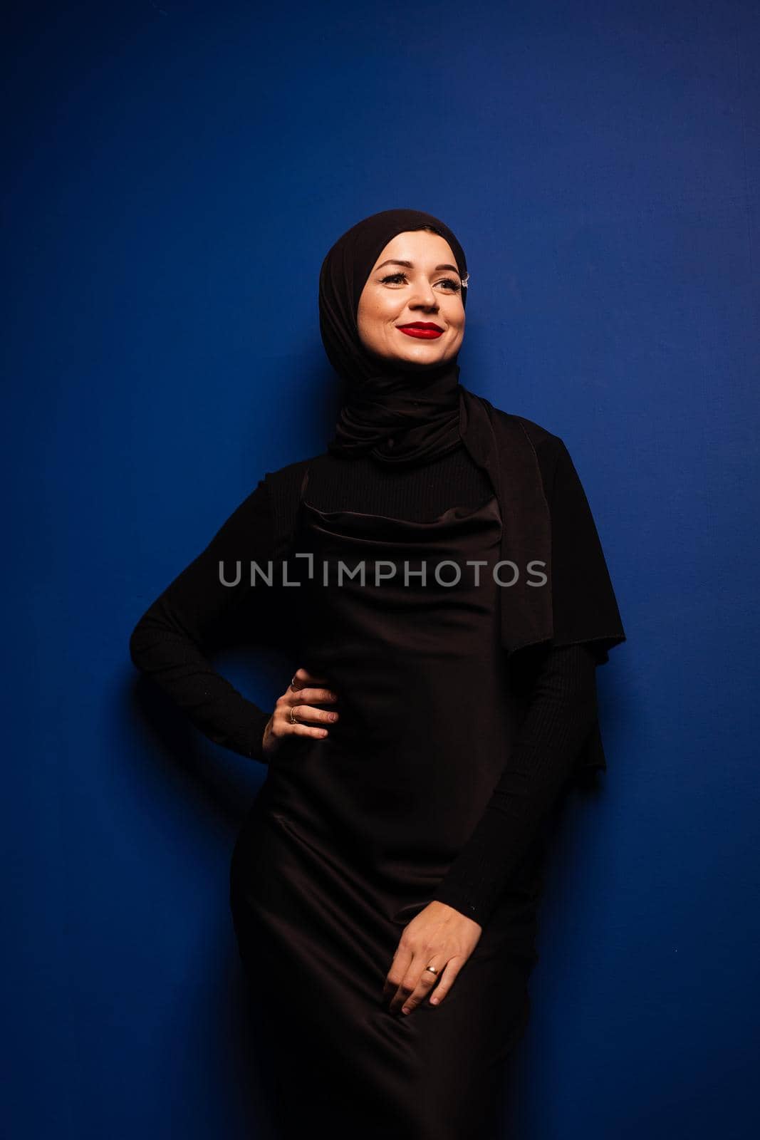 Fashion muslim model in black hijab is posing on blue background in studio. Islam religion