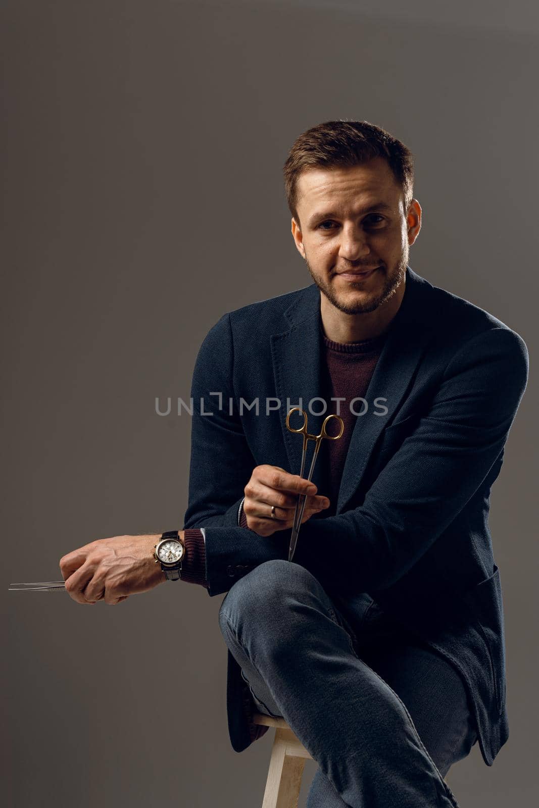 Doctor with surgical equipment needle and scissors. Handsome man weared casual business suit. Portrait of surgeon in studio