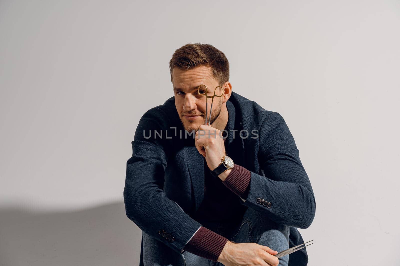 Doctor with surgical equipment needle and scissors. Handsome man weared casual business suit. Portrait of surgeon in studio