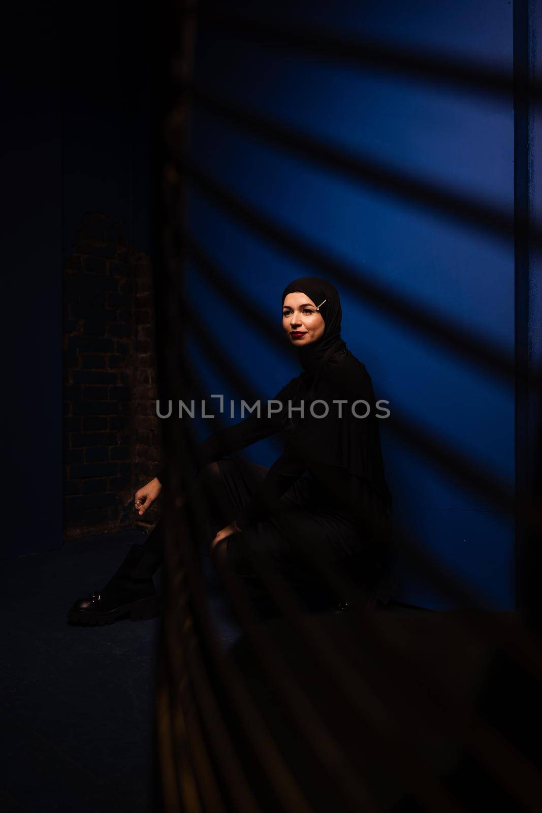 Fashion muslim model in black hijab is posing on blue background in studio. Islam religion creative photo.