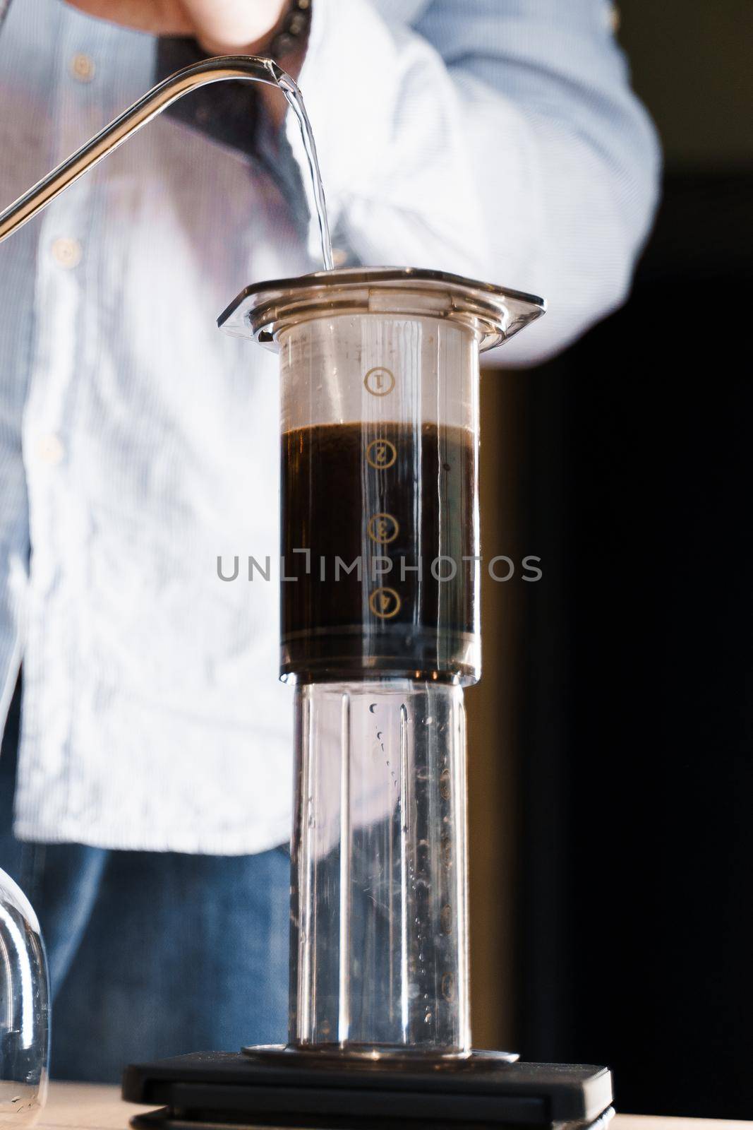 Aeropress coffee close up alternative making by barista in the cafe vertical photo. Barista pours hot water in pot for making aeropress coffee. by Rabizo