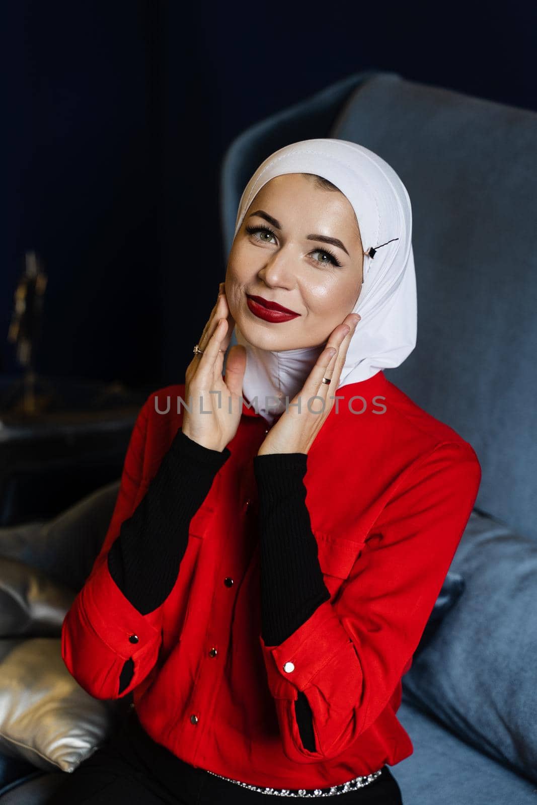 Attractive muslim caucasian girl weared head scarf is sitting on the sofa. Islam religion