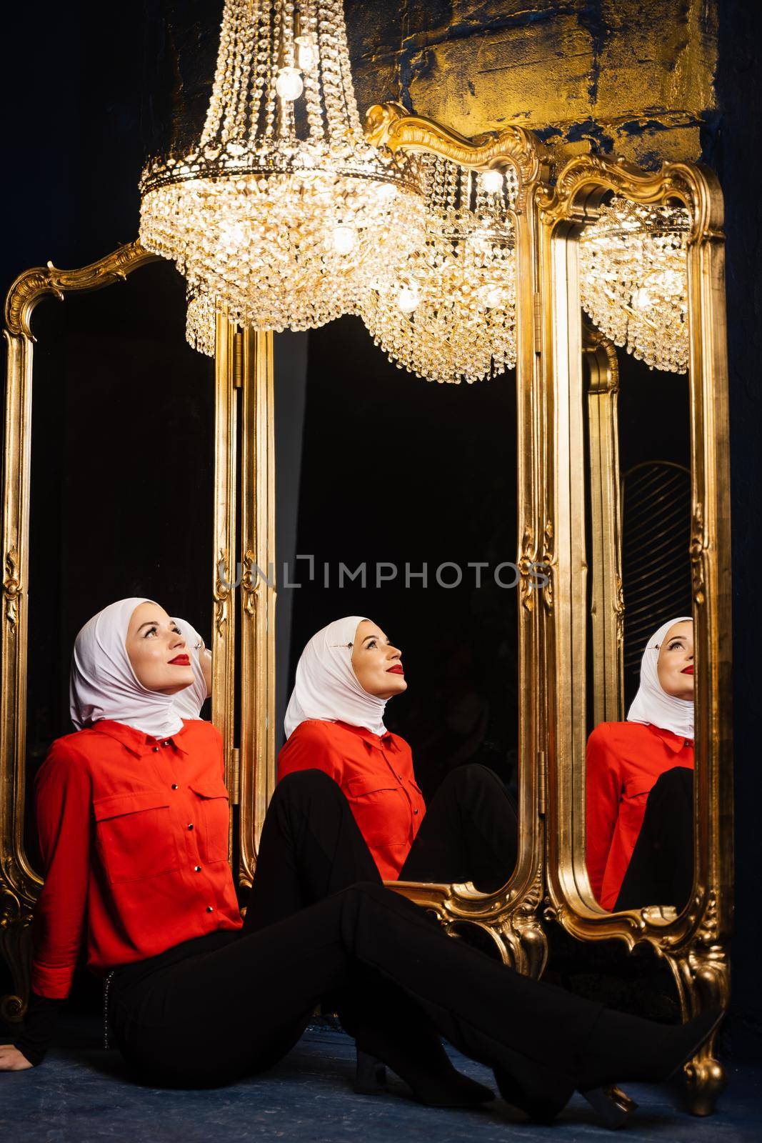 Muslim girl near mirrors with her reflections. Fashion muslim model near big expensive chandelier. Islamic religion