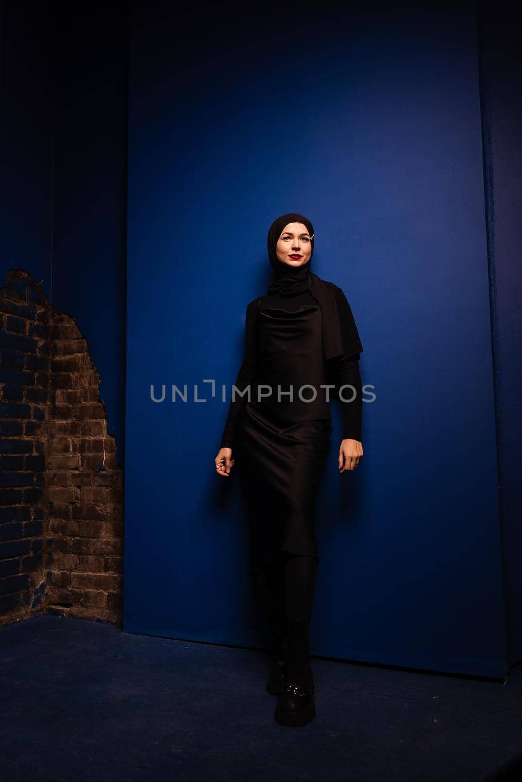 Fashion muslim woman in black hijab is posing on blue background in studio. Professional caucasian model. by Rabizo