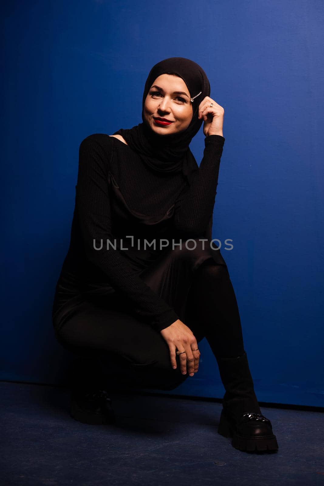 Fashion muslim model in black hijab is posing on blue background in studio. Islam religion