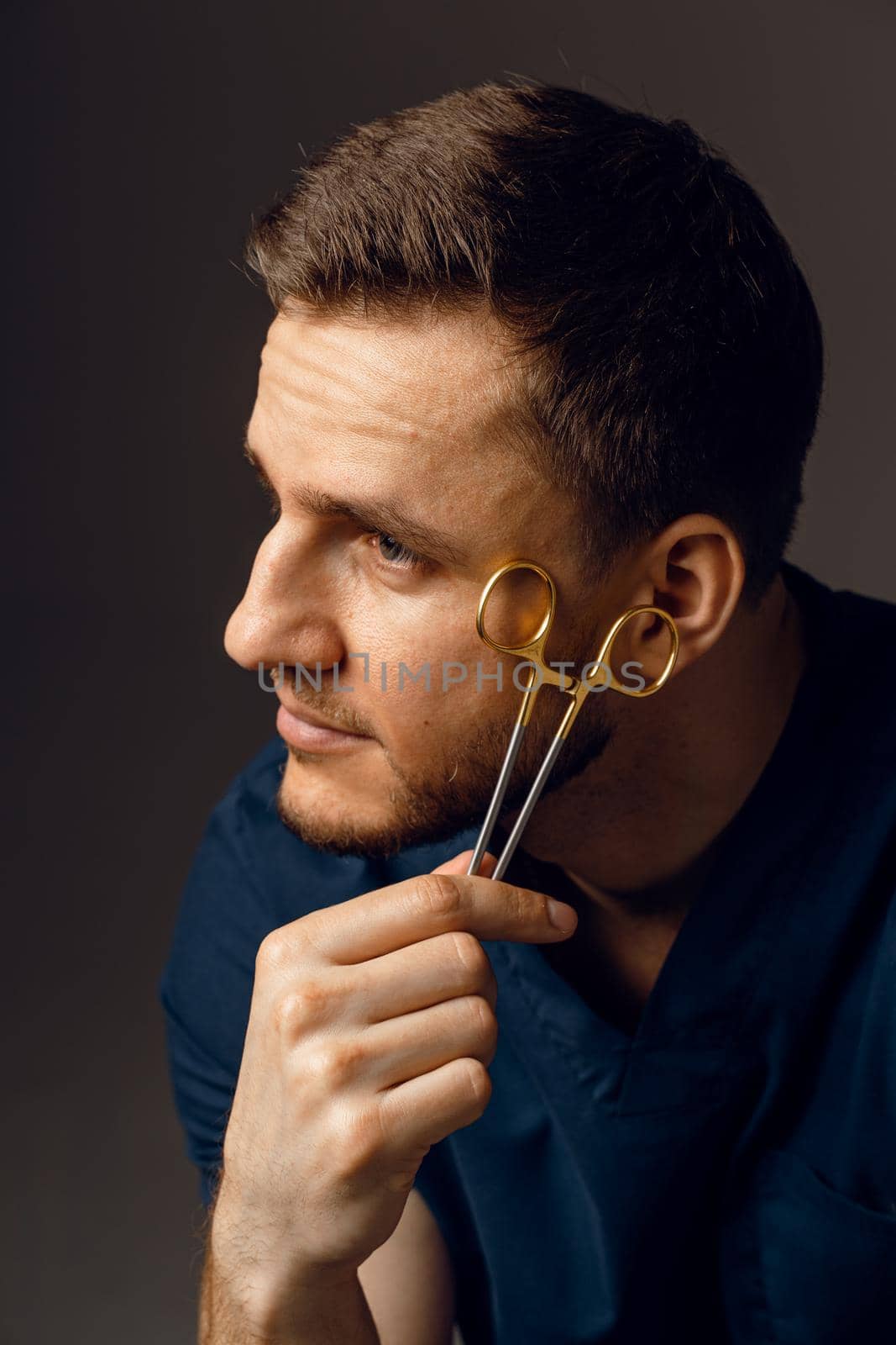 Handsome doctor with surgical scissors close-up. Confident man holding medical equipment in hands and smiling. Happy male posing in studio