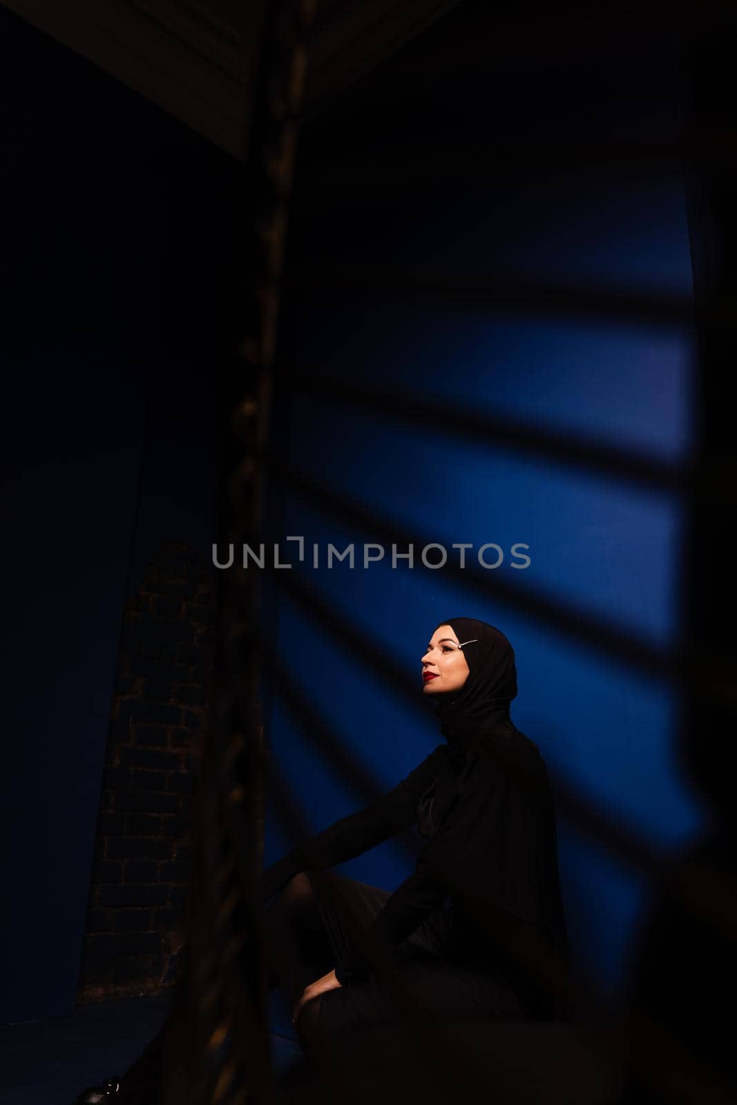 Fashion muslim model in black hijab is posing on blue background in studio. Islam religion creative photo.