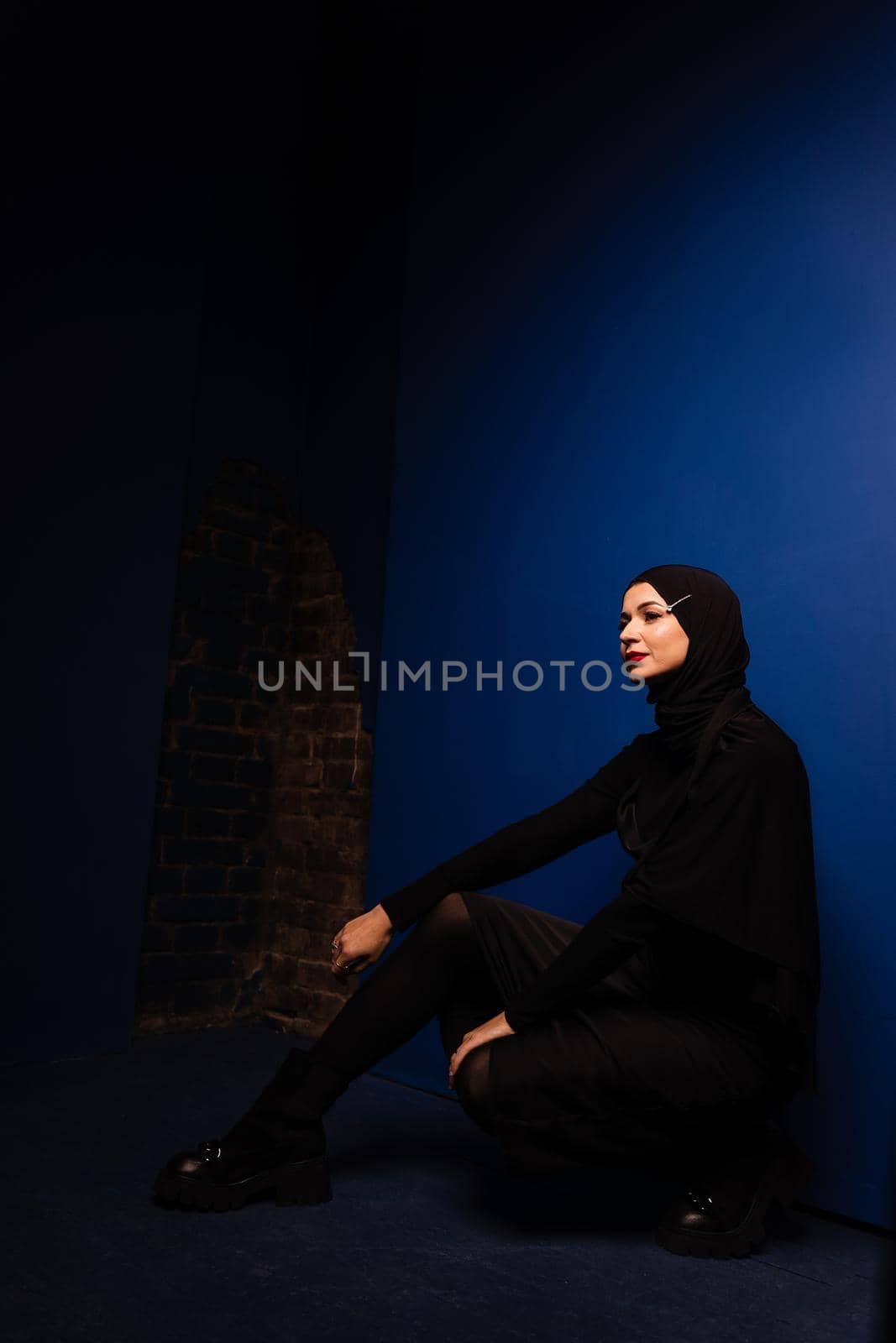 Fashion muslim model in black hijab is posing on blue background in studio. Islam religion creative photo.