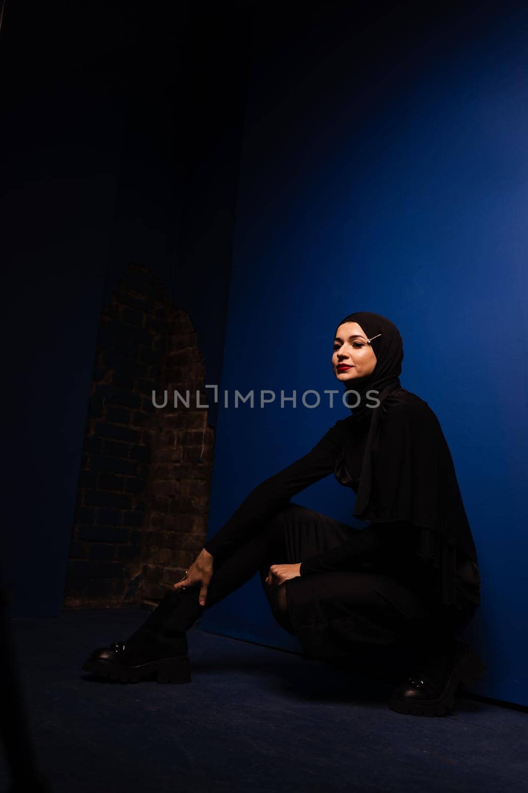 Fashion muslim model in black hijab is posing on blue background in studio. Islam religion creative photo.