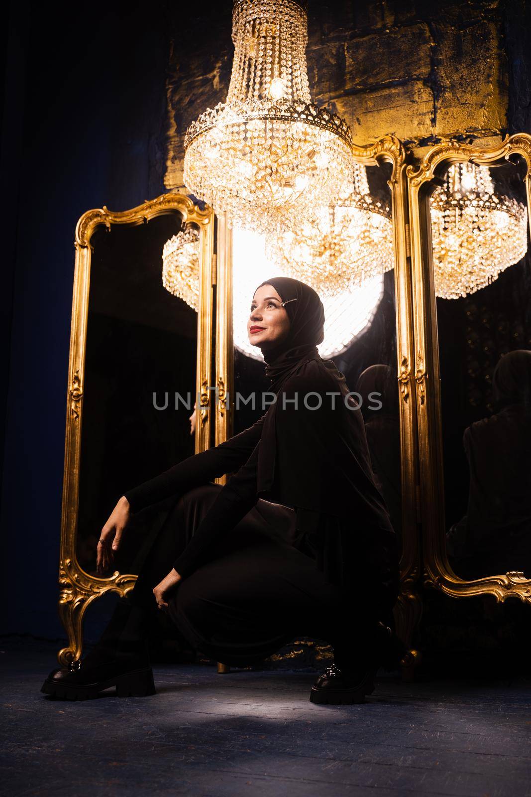 Muslim girl in black hijab near mirrors with her reflections. Fashion muslim model near big expensive chandelier. Islamic religion. by Rabizo