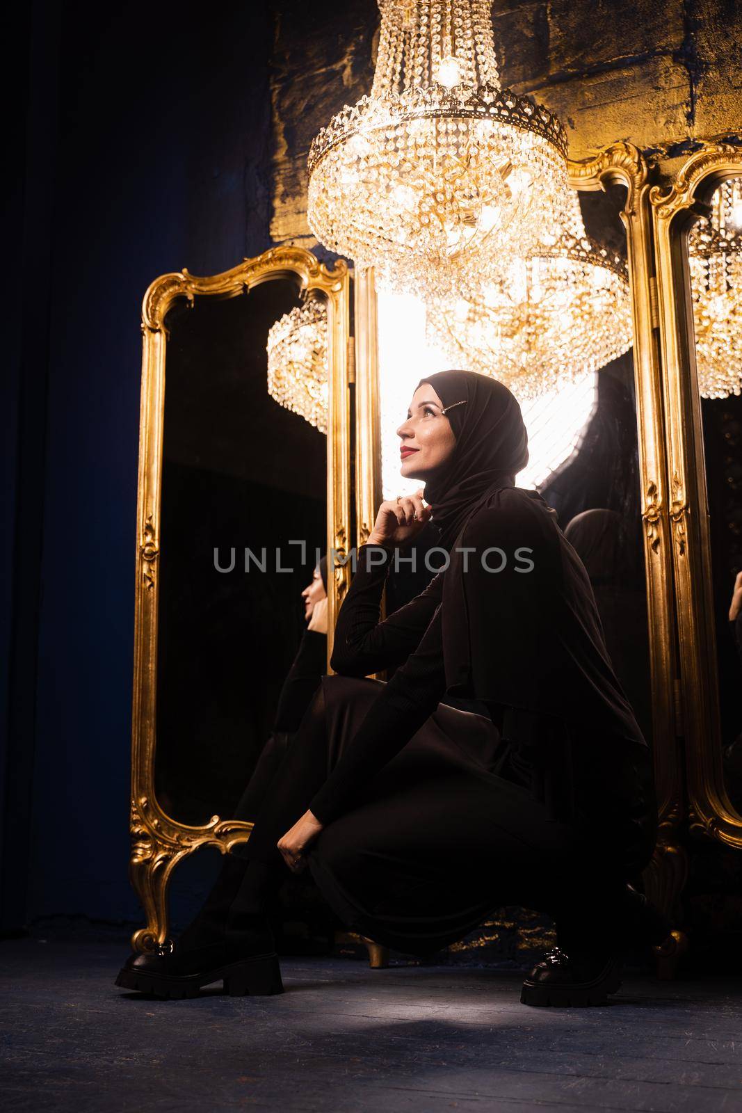 Muslim girl in black hijab near mirrors with her reflections. Fashion muslim model near big expensive chandelier. Islamic religion. by Rabizo