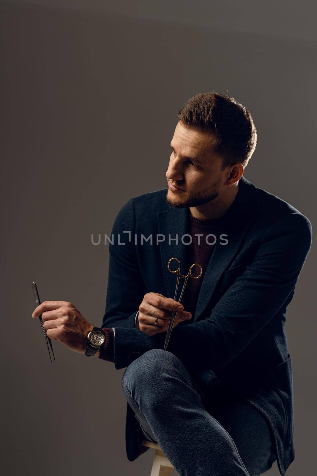 Doctor with surgical equipment needle and scissors. Handsome man weared casual business suit. Portrait of surgeon in studio