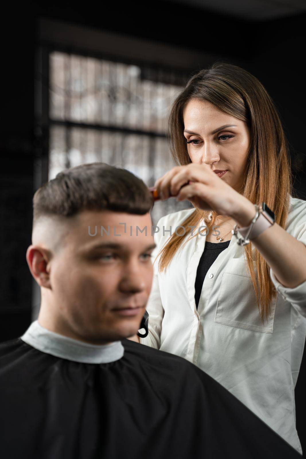 Woman barber making hairstyle in barbershop using clipper. Hairdresser cutting hair of handsome man. by Rabizo