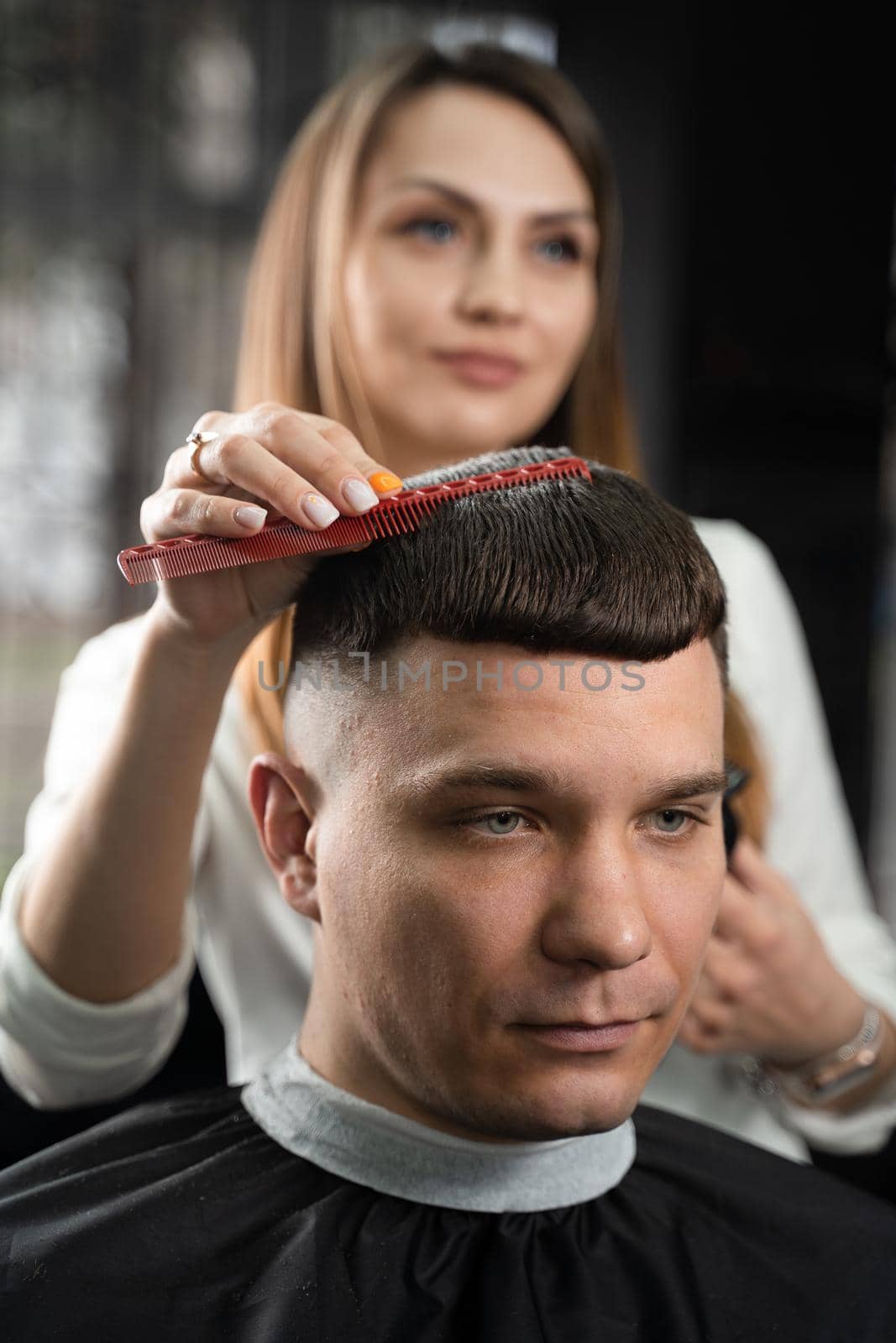 Woman barber making hairstyle in barbershop using clipper. Hairdresser cutting hair of handsome man