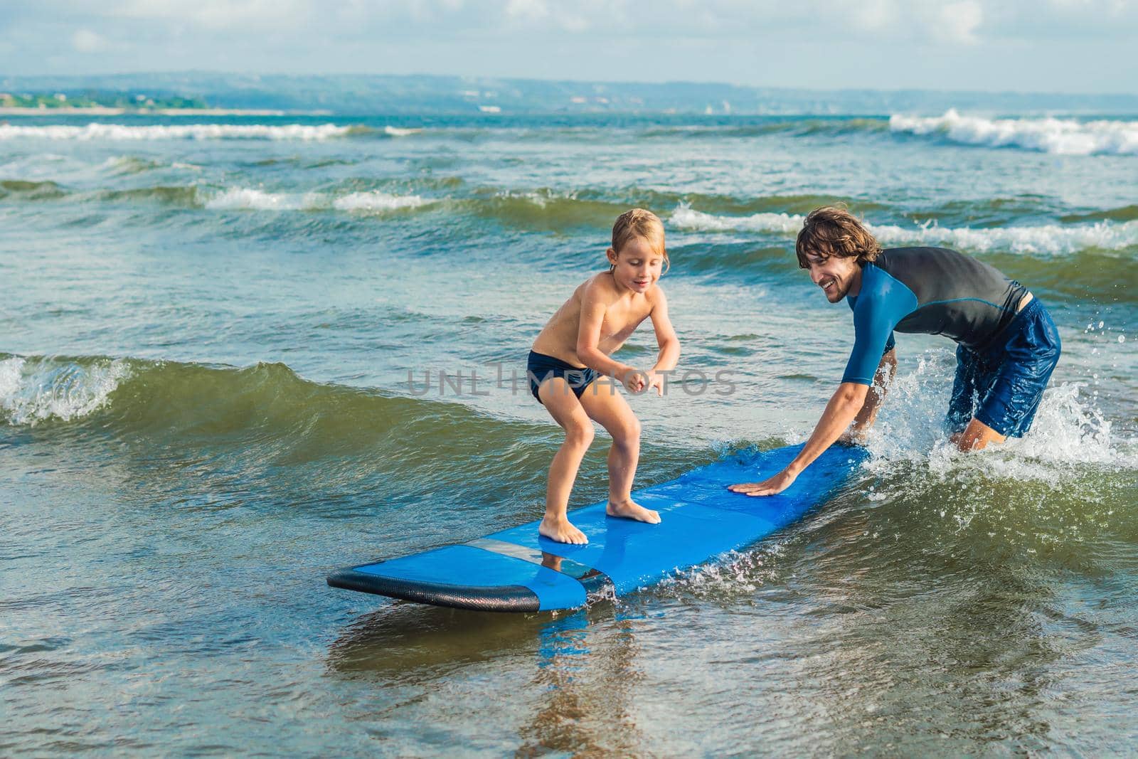 Father or instructor teaching his 4 year old son how to surf in the sea on vacation or holiday. Travel and sports with children concept. Surfing lesson for kids.