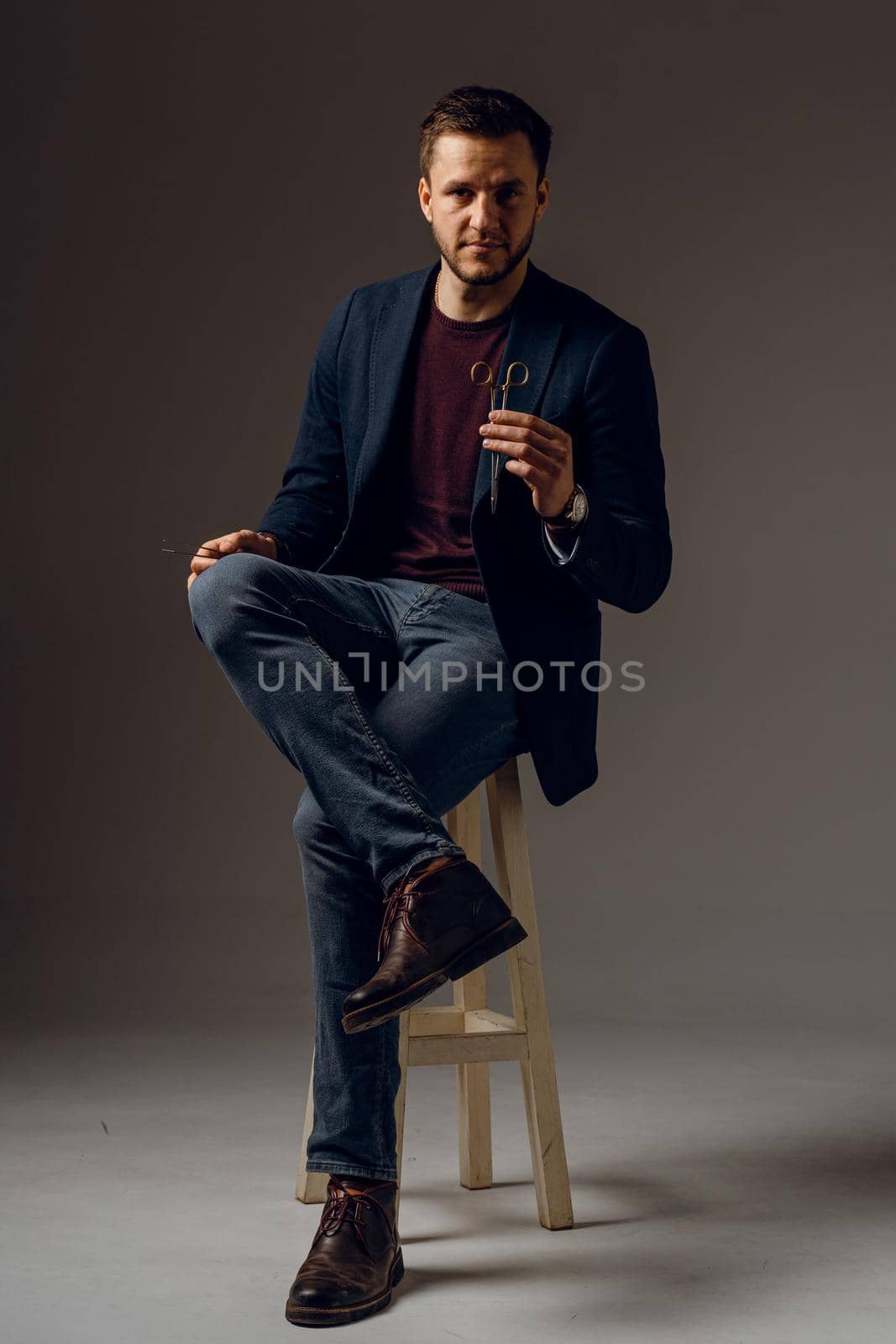 Handsome surgeon with needle holder and surgical knife weared casual suit in studio. Confident business man on dark background