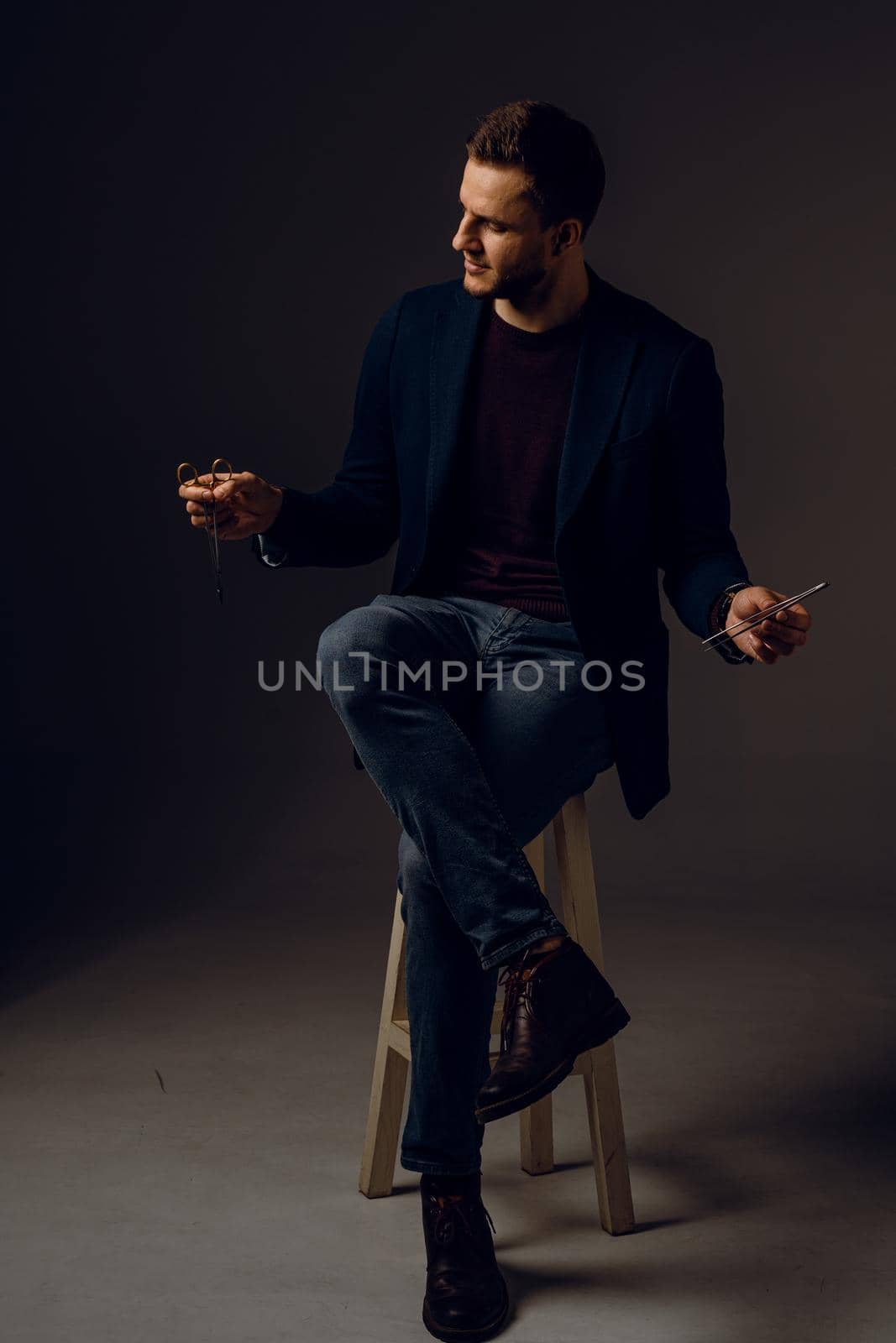 Handsome surgeon with needle holder and surgical knife weared casual suit in studio. Confident business man on dark background