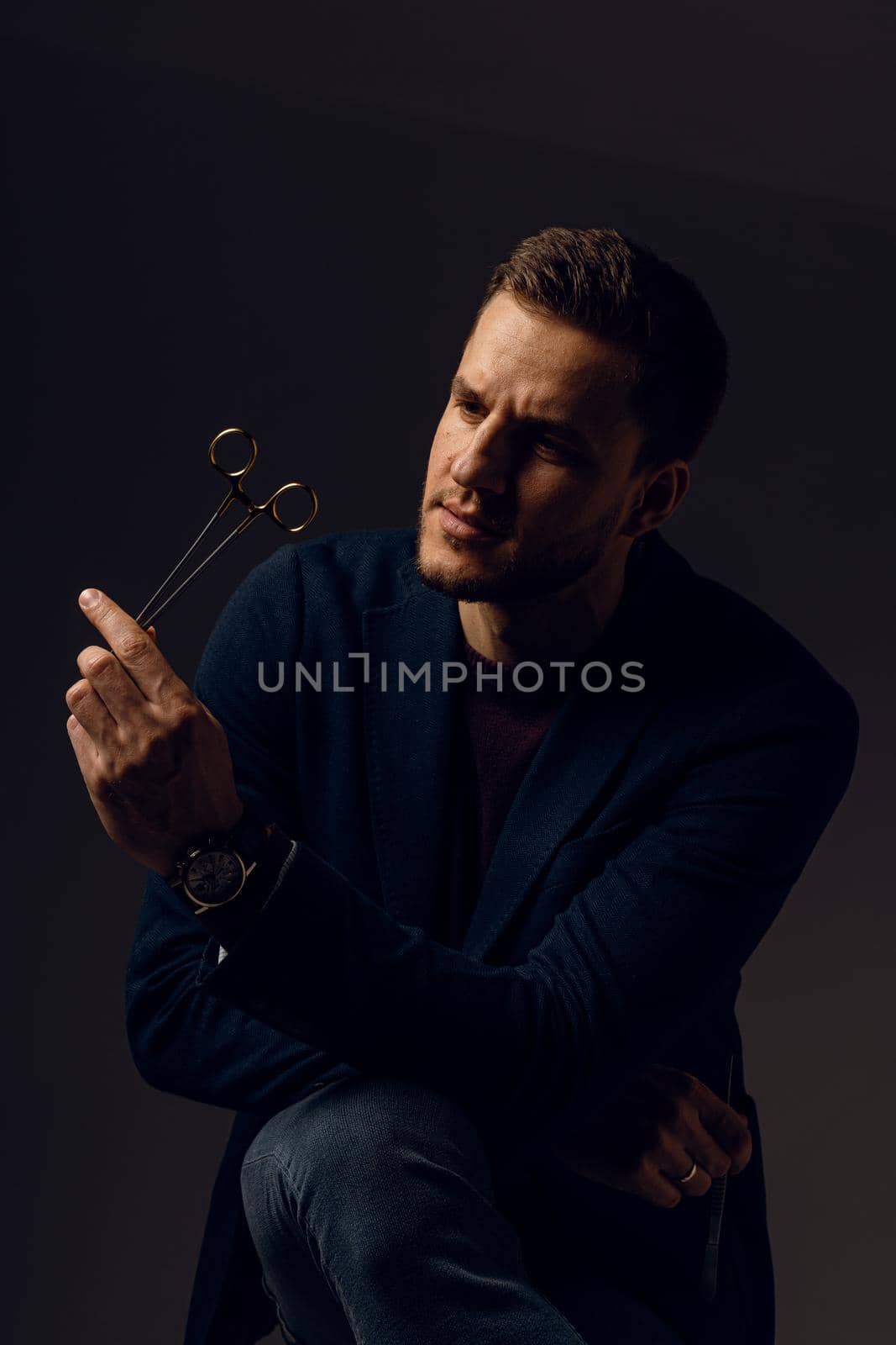 Doctor with surgical equipment needle and scissors. Handsome man weared casual business suit. Portrait of surgeon in studio