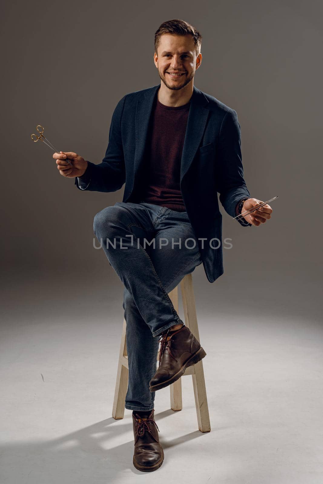 Handsome surgeon with needle holder and surgical knife weared casual suit in studio. Confident business man on dark background