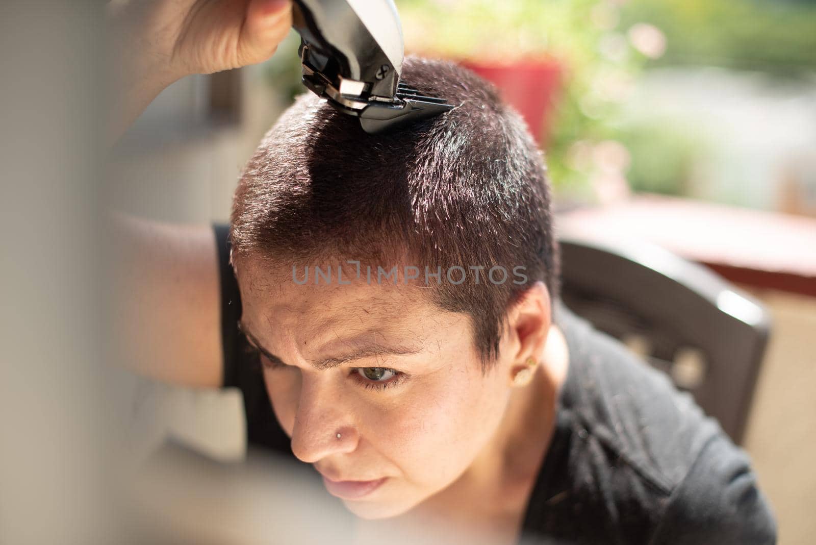 worried young woman shaving your hair head with a razor machine and smiling at home, horizontal high quality photo
