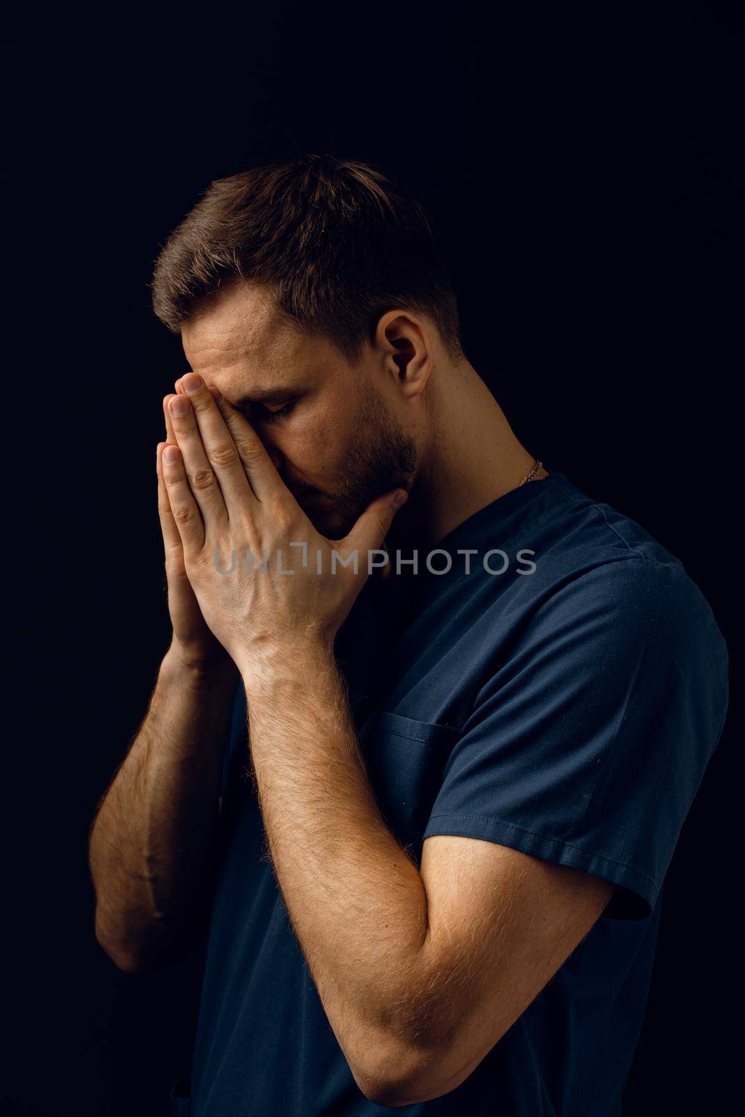 Handsome man pray and believe in God. Orthodox Christian faith. Man cover his face with his hands and thinks about life. by Rabizo