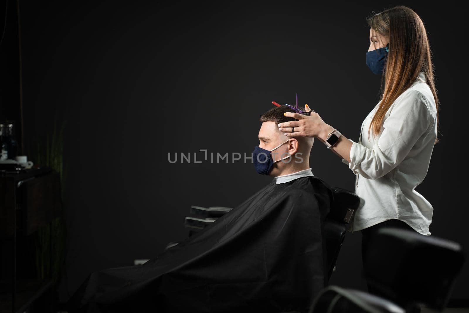 Barbershop service at coronavirus covid-19 period. Woman barber making hair for handsome man. Using mask. by Rabizo