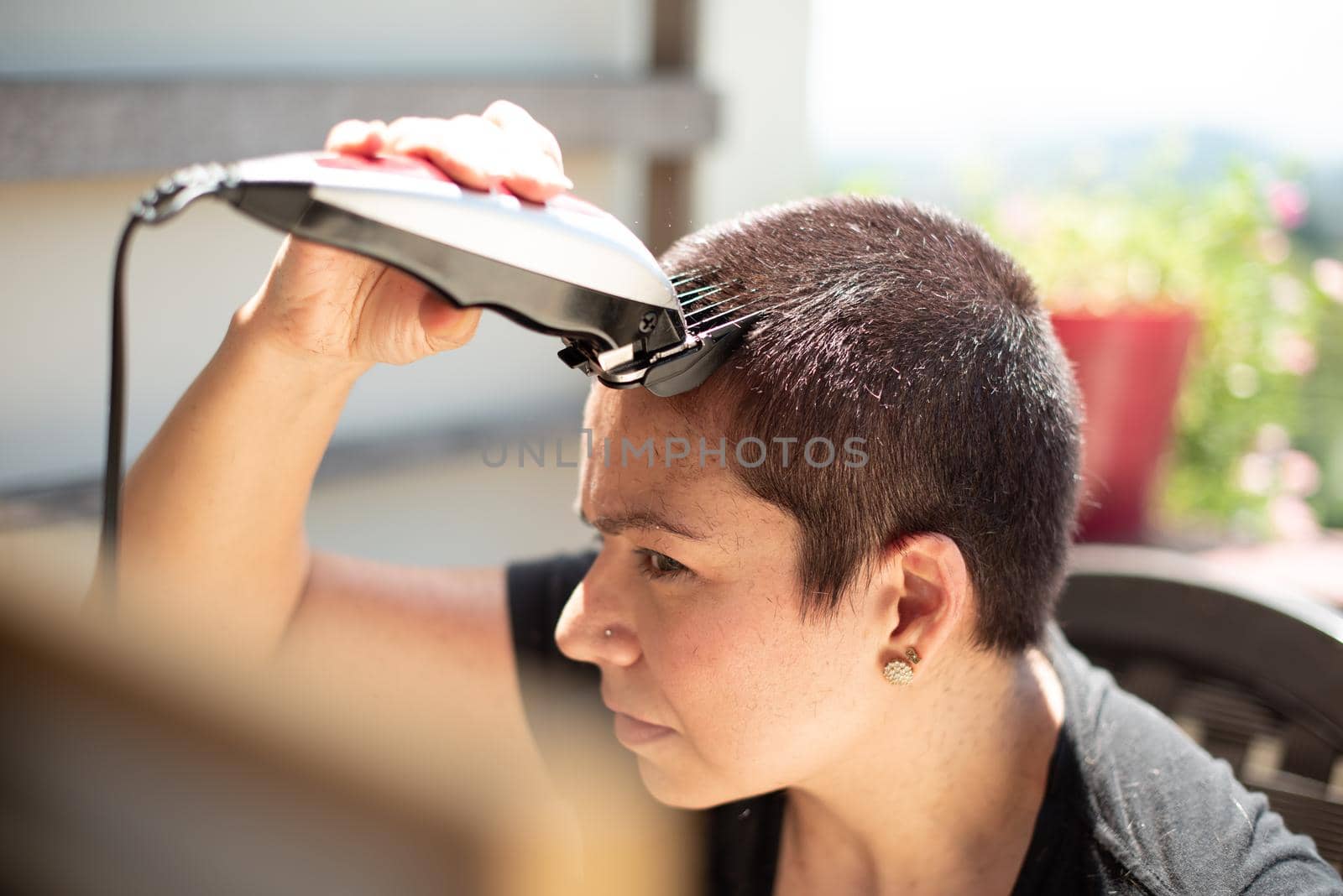 worried young woman shaving your hair head with a razor machine and smiling at home, horizontal high quality photo