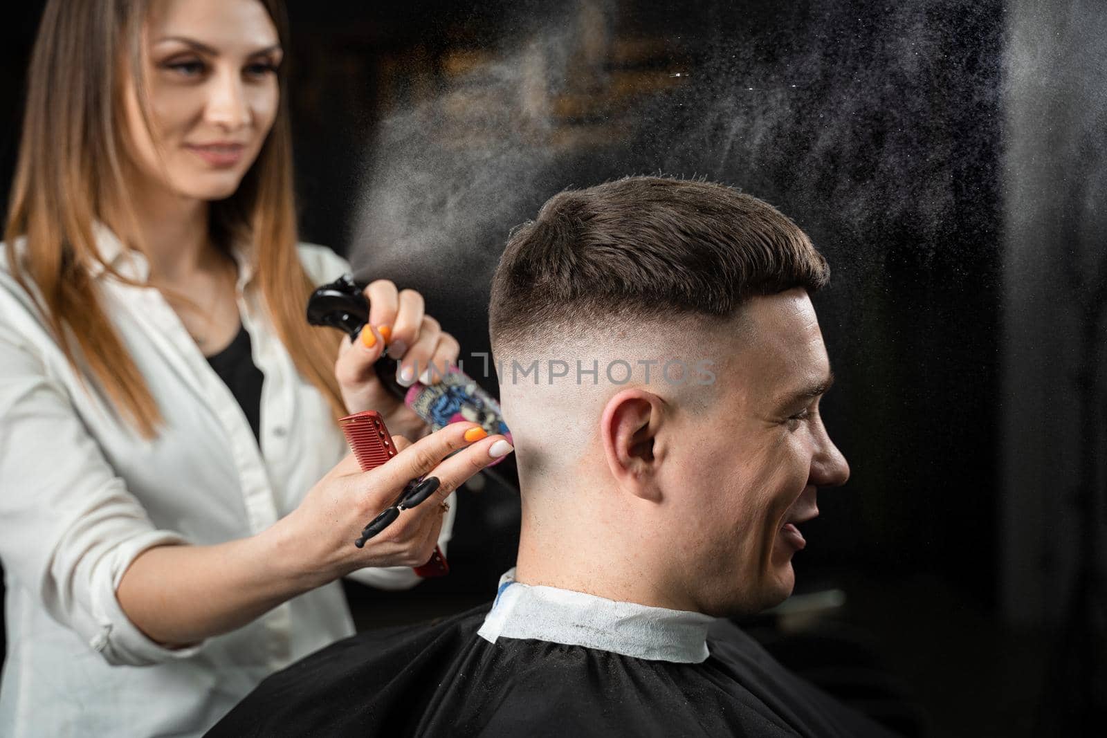 Woman barber making hairstyle in barbershop using clipper. Hairdresser cutting hair of handsome man