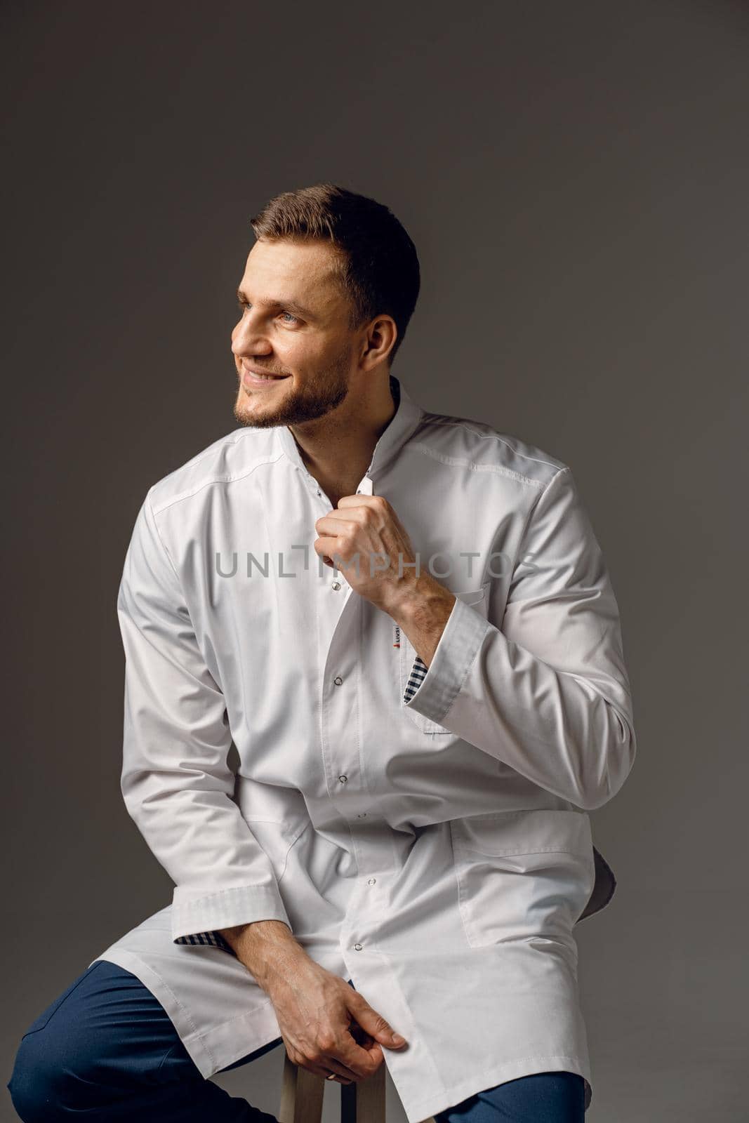 Surgeon weared in medical robe smile on dark background. Handsome happy doctor posing in studio